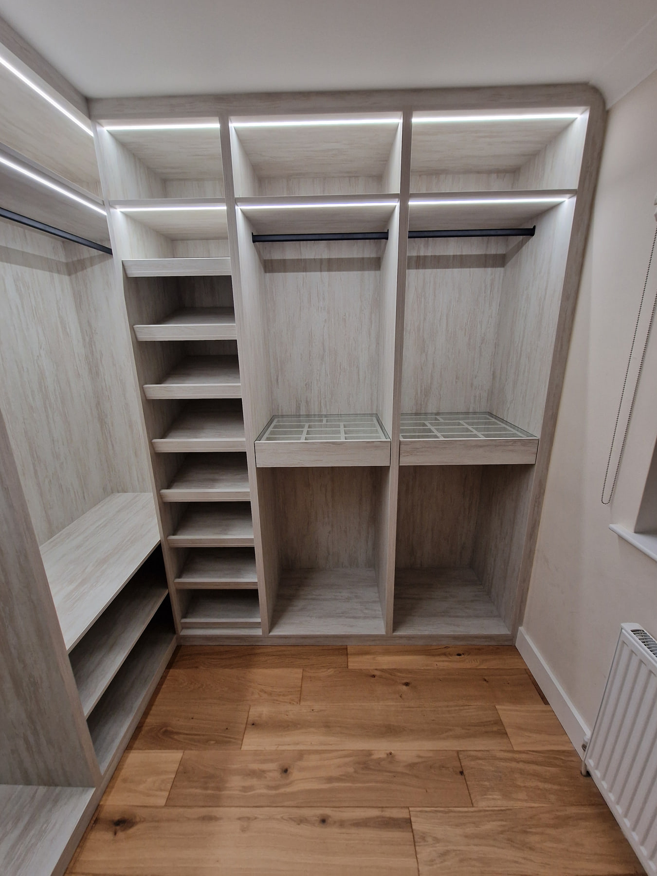 Completed light woodgrain walk-in wardrobe with illuminated shelves and black hanging rails
