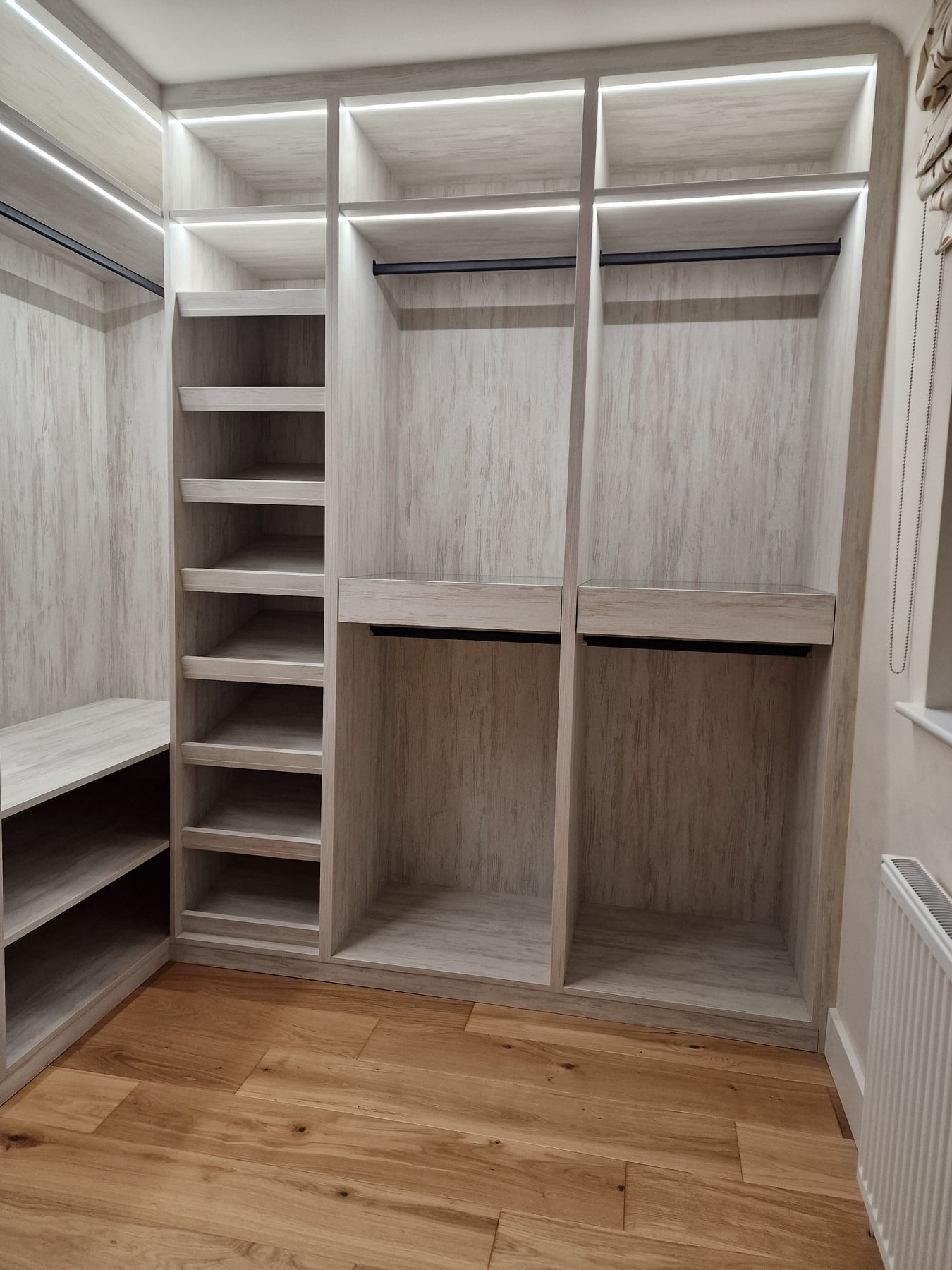 Completed light woodgrain walk-in wardrobe with illuminated shelves and black hanging rails